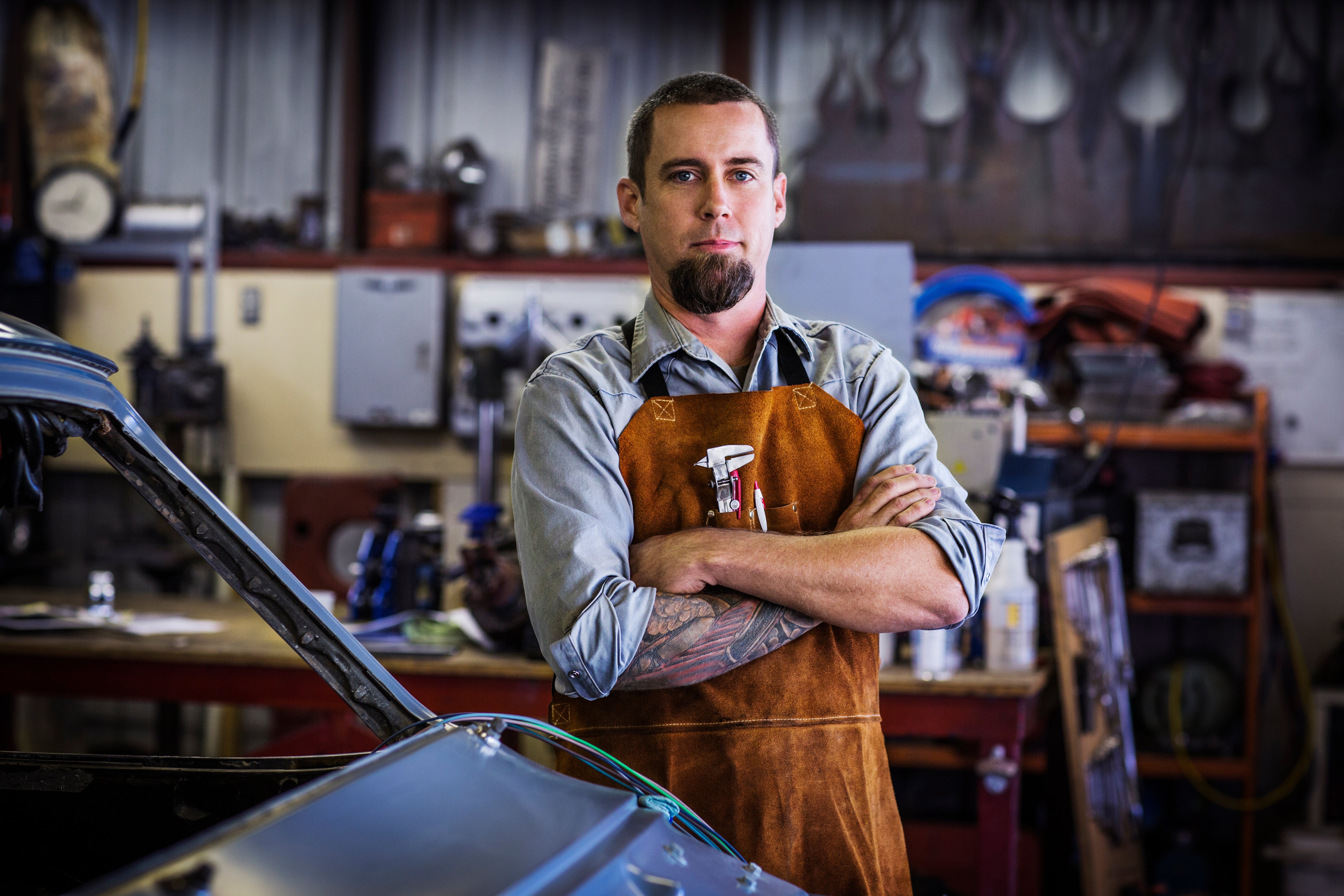 Mechanic with a full goatee standing with arms cross